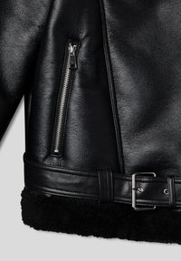 Giubbotto in pelle nera con tasca con zip, ampio colletto in shearling nero e cintura con fibbia argentata in vita. Superficie testurizzata.