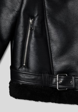 Czarna skórzana kurtka z zamkniętą kieszenią, szerokim czarnym kołnierzem z baraniej wełny i paskiem z srebrną klamrą w talii. Teksturowana powierzchnia.