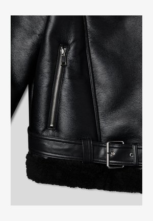 Czarna skórzana kurtka z zamkniętą kieszenią, szerokim czarnym kołnierzem z baraniej wełny i paskiem z srebrną klamrą w talii. Teksturowana powierzchnia.