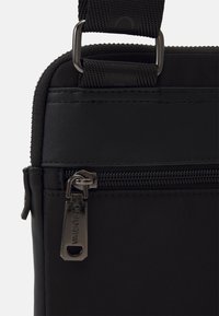 Borsa in tessuto nero con scomparto con cerniera, finitura testurizzata e dettagli in metallo. Tracolla regolabile per il trasporto.