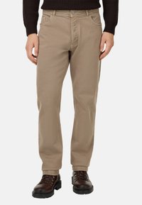 Pantalones de algodón en tono beige con un corte recto, que cuentan con bolsillos frontales y cremallera. Combinados con botas marrón oscuro con cordones.