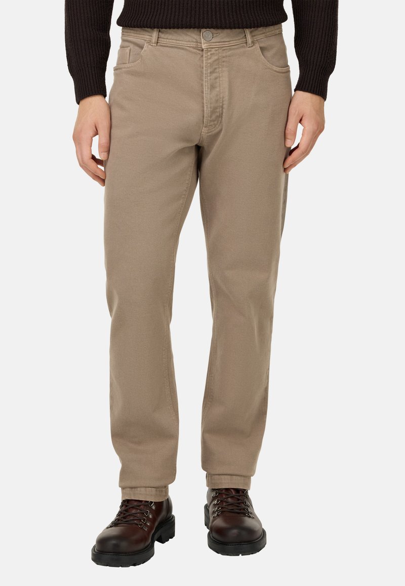 Pantalones de algodón en tono beige con un corte recto, que cuentan con bolsillos frontales y cremallera. Combinados con botas marrón oscuro con cordones.