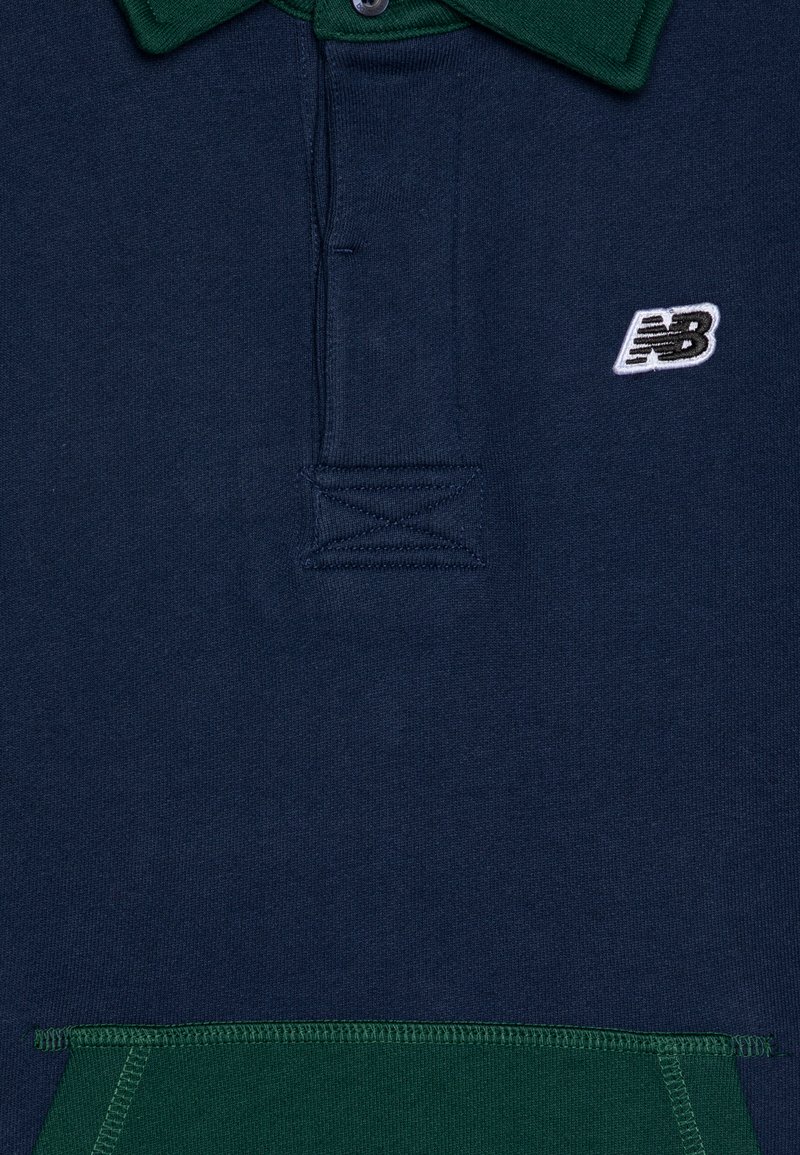 Marineblauwe polo met een groene kraag, voorzien van een twee-knops sluiting en een witte geborduurde New Balance-logo op de linkerkant van de borst.
