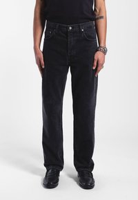 Jeans de mezclilla negra con cintura alta, corte recto, bolsillos frontales visibles y un sutil desvanecimiento. Se llevan con zapatos negros.