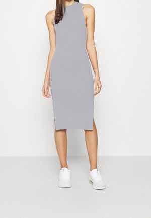 Woman wearing a sleeveless, ribbed, knee-length gray dress paired with white athletic sneakers, standing against a plain white background.