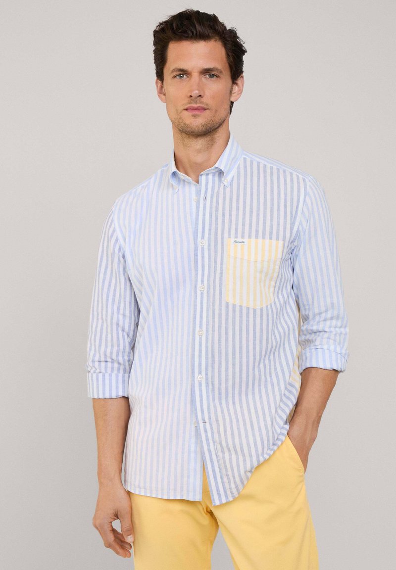 Camisa de botones a rayas en azul claro y blanco, con un bolsillo en el pecho amarillo. Las mangas largas están arremangadas y la tela parece suave.