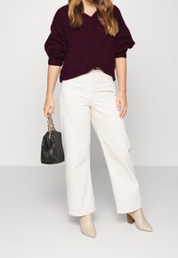 Burgunderröd oversized stickad tröja med V-ringning, kombinerad med vita vida byxor. Matchas med en svart plisserad handväska och beige klackar.