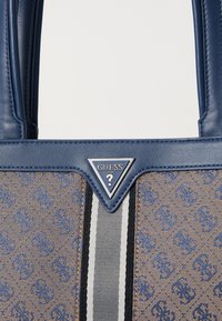 Sac à main synthétique bleu avec un panneau décoratif en brun texturé, accent logo en argent et rayures verticales en noir et gris.