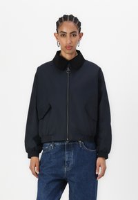 Black zip-up bomber jacket with a corduroy collar, elastic cuffs, and two front pockets. Worn with blue denim jeans.