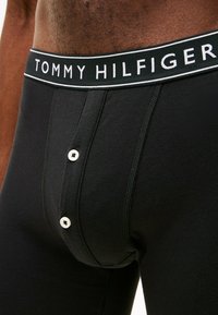 Boxer in cotone nero con un elastico in vita bianco con il logo "TOMMY HILFIGER", dotati di un frontale con bottone e dettagli di cucitura a contrasto.