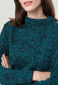 Pull en tricot à col montant, de couleur noire, avec un motif texturé en vert lagon, des manches longues et une coupe décontractée.
