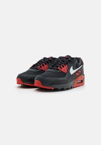 Sneakers Nike Air Max con una parte superiore in rete e suede nera, dettagli rossi e un'unità di ammortizzazione ad aria visibile nella suola.