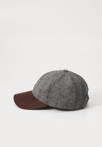 Sapcă cu model houndstooth gri, având o margine din suede maro. Dispune de șase panouri și un buton de sus, oferind un design structurat.