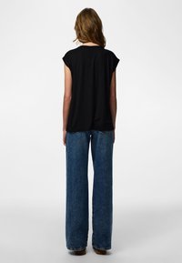 Fekete, rövid ujjú felső laza szabással, széles szárú kék farmernadrággal, amely texturált felülettel és klasszikus varrási részletekkel rendelkezik.