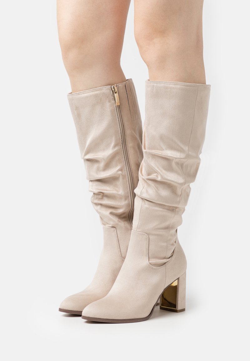 Beige kniehohe Stiefel mit einem lässigen Design, aus weichem Wildleder, mit einem seitlichen Reißverschluss und einem klobigen, goldakzentuierten Absatz.