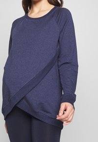 Felpa navy con design frontale diagonale, tessuto morbido, maniche lunghe e polsini a costine, abbinata a leggings scuri.