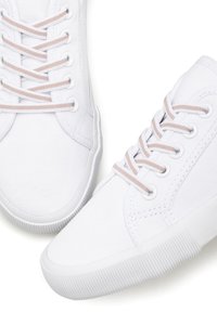 White canvas sneakers featuring a low-top design, textured surface, and light pink laces. Rubber outsole with a ridged pattern for grip.