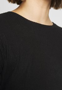 Top nero a costine con scollo rotondo. Il tessuto ha una texture liscia e linee verticali, creando un motivo sottile. Viste ravvicinate.