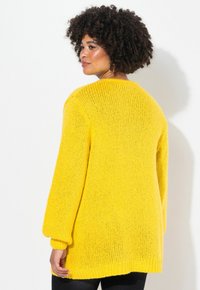 Svetro giallo lavorato a maglia in oversized con maniche lunghe, caratterizzato da un motivo testurizzato e un collo rotondo. La vista posteriore mostra una silhouette rilassata.