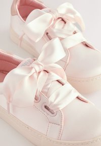 Hellrosa Sneaker aus glattem Material, mit breiten Satinbändern als Schnürsenkel und einer strukturierten Sohle. Einfaches und modernes Design.