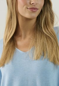 Svetlo modrý pletený sveter s výstrihom do V. Mäkká textúra, dlhé rukávy a minimálne detaily. Vhodný na neformálne nosenie.