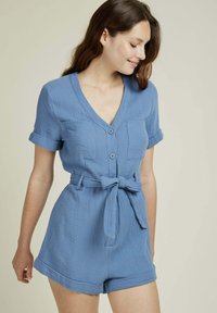 Rompers bleu clair à manches courtes en tissu texturé, avec un col en V, deux poches sur le devant et une ceinture à nouer à la taille pour un look ajusté.
