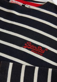 Sötétkék és fehér csíkos pamut felső, kerek nyakú, piros hímzett "SuperDry" logóval a mellkason.