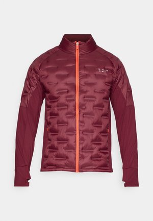 Tumši sarkans polsterēts jaka ar oranžu rāvējslēdzēju, augstu apkakli un garām piedurknēm. Izceļas ar teksturētu priekšpusi un gludu piedurkņu audumu.