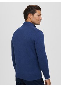 Maglione lavorato a maglia blu navy con colletto alto, polsini e orlo a coste, caratterizzato da una texture liscia e un design aderente.