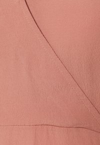 Tkanina w kolorze brzoskwiniowym o drobnej teksturze i subtelnej poświacie. Posiada skośne szwy i lekki, drapowany wygląd.