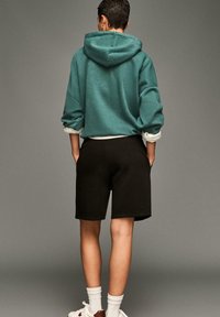 Zöldeskék, oversize kapucnis pulóver, feltekerhető ujjakkal, fekete rövidnadrággal párosítva, mindkettő puha anyagból készült. A megjelenést fehér zoknik és sportcipők teszik teljessé.