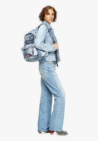 Denim jacket and flared jeans in light blue wash, paired with a patterned gray backpack and black shoes with red heels.