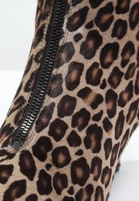 Stivale alla caviglia con stampa leopardata e una zip nera, realizzato in materiale a trama morbida. Presenta distintivi motivi marrone scuro e chiaro.