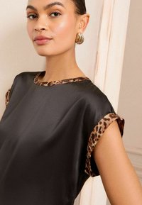 Černý saténový top s rukávy a výstřihem s leopardím vzorem. Má uvolněný střih a hladkou texturu. Jednoduchý, elegantní design.