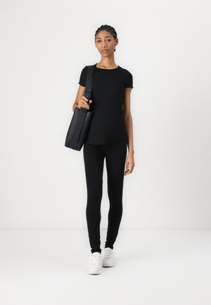 Zwarte geribde top met korte mouwen, gecombineerd met zwarte leggings en witte sneakers. Draagt een zwarte, gestructureerde handtas met een lange schouderband.