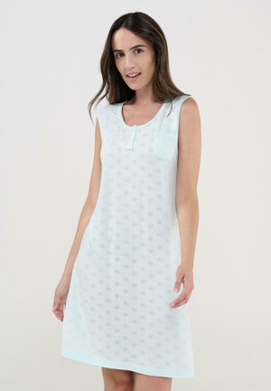 Mujer con camisón sin mangas azul claro con patrón de estrellas y pequeño bolsillo en el pecho, de pie contra un fondo liso.