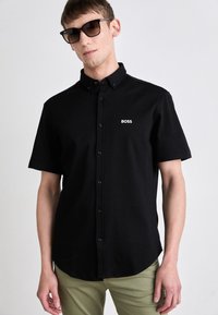 Camicia nera a maniche corte con bottoni e colletto a punta, con il logo bianco "BOSS" sul lato sinistro del petto. Tessuto liscio, vestibilità classica.