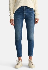 Blå slim jeans med normal midja, med en slät textur och lätt blekning vid låren. Matchas med krämfärgade sneakers.