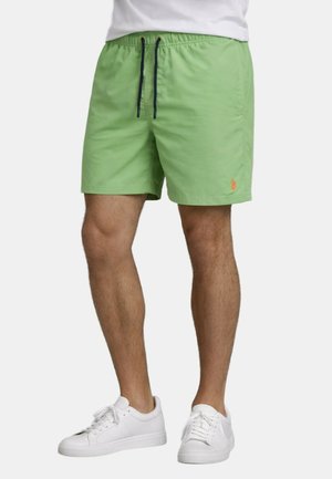 Mann trägt hellgrüne Shorts mit Kordelzug und weiße Sneaker, steht vor einem schlichten Hintergrund.