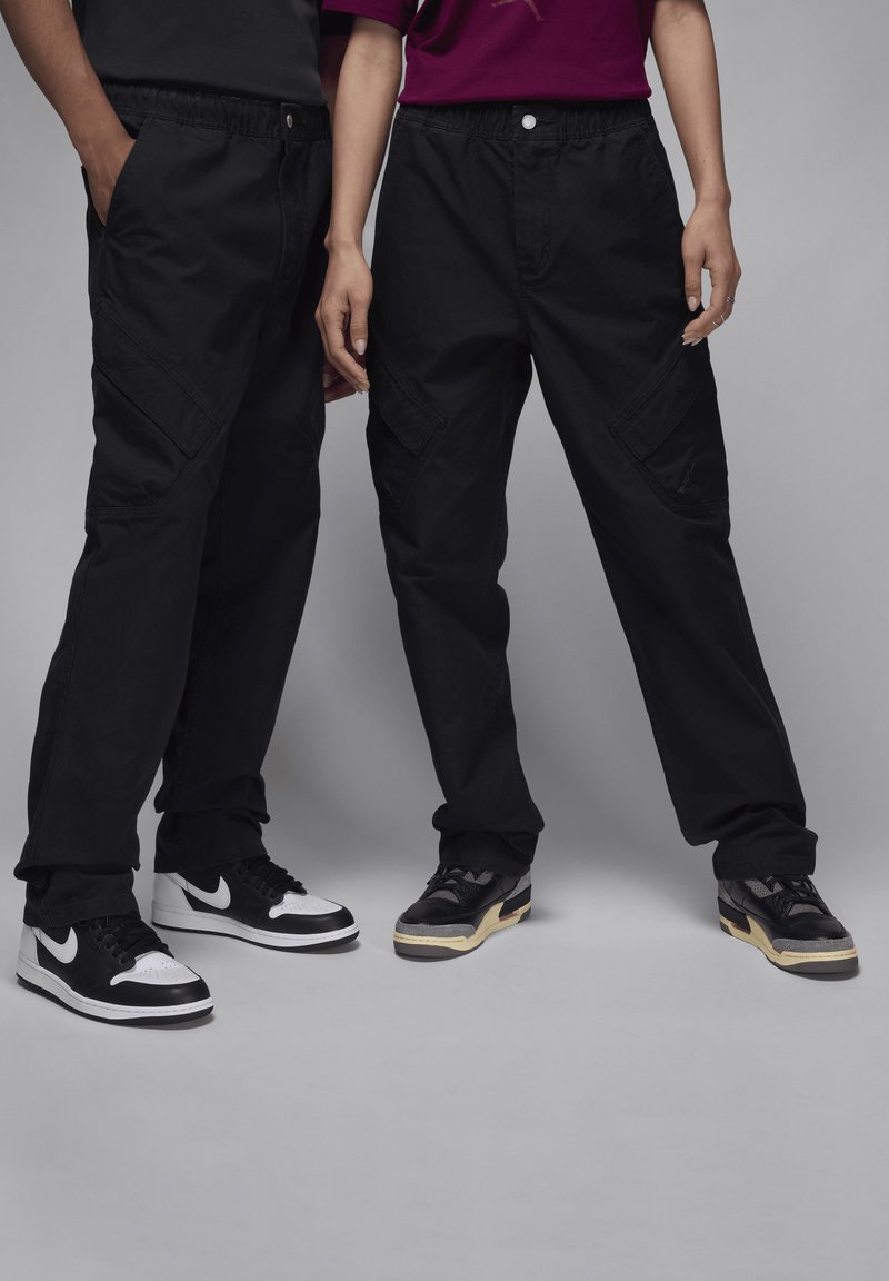 Pantalones cargo oversized negros con cinturilla elástica y bolsillos laterales, combinados con zapatillas negras y blancas. Tejido suave, silueta rectangular.