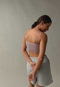 Top corto lilla a coste con spalline sottili, abbinato a pantaloncini grigio chiaro. Il design presenta una texture liscia e una silhouette aderente.