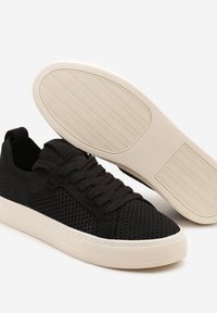 Baskets noires en mesh avec lacets noirs plats, semelle en caoutchouc blanc dotée d'un motif de grip texturé et conception basse.
