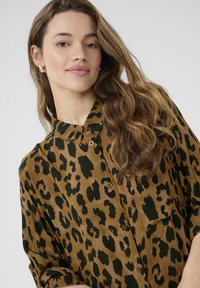 Chemise à boutons imprimée léopard dans des tons de marron et de vert, avec un col, des détails de boutons et une coupe décontractée avec des manches retroussées.