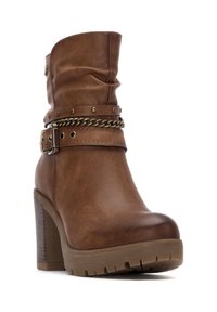 Stivale alla caviglia in finta pelle marrone con tacco spesso, al collo morbido e una cinghia borchiata con un accento a catena. Suola in gomma spessa con trazione.