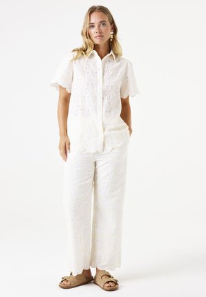 White cotton button-up shirt with short sleeves, featuring intricate floral embroidery and cut-out details, paired with matching wide-leg pants.