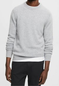 Grau melierter Rundhalsausschnitt-Pullover aus weichem Stoff mit gerippten Bündchen und Saum, getragen über einem weißen Hemd, kombiniert mit dunklen Hosen.