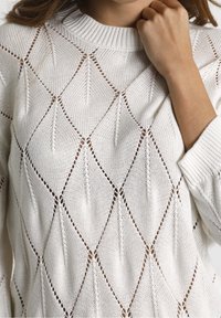 Valkoinen neulepaita, jossa on timanttikuvio ja avoin ommel. Ribbauskaulus ja hihansuut, kevyt rakenne.