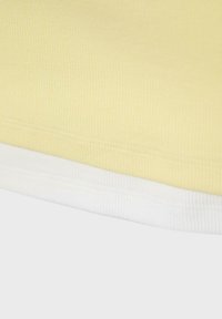 Lähikuva poimutetun vaaleankeltaisen ja valkoisen kankaan reunoista, joista on näkyvissä saumanompeleet vaatteessa.