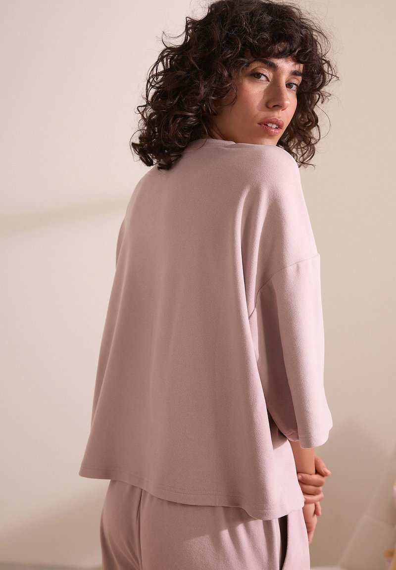 Maglietta oversize rosa chiaro con un taglio morbido, texture soffice e maniche a trequarti, indossata con un pantalone abbinato, vista da dietro.