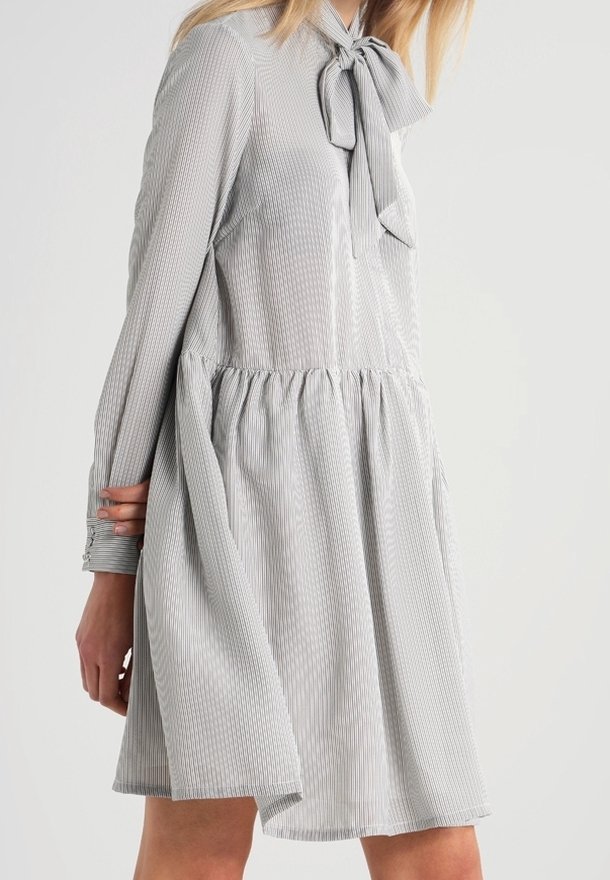 Randig klänning i ljusgrått med rosett vid kragen, långa ärmar och insvängd midja, med en flödande kjol och mjuk textur.